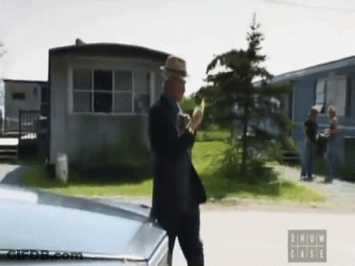 A Man In A Suit And Hat Is Standing Next To A Car With The Words Show Case On The Bottom Left GIF