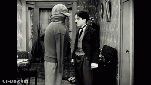 A Man In A Suit And Hat Is Standing Next To Another Man In A Room . GIF