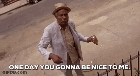 A Man In A Suit And Hat Is Standing On A Sidewalk Holding A Can Of Soda And Talking To Someone . GIF
