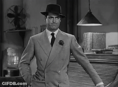 A Man In A Suit And Hat Is Standing With His Hands In His Pockets . GIF