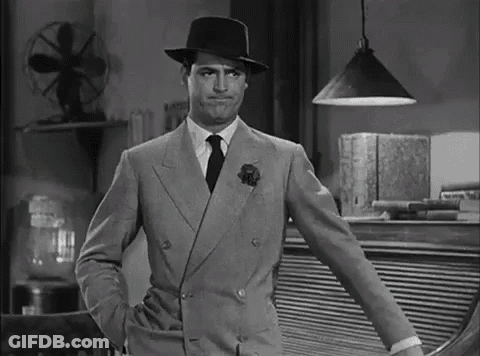 A Man In A Suit And Hat Is Standing With His Hands In His Pockets In A Black And White Photo . GIF