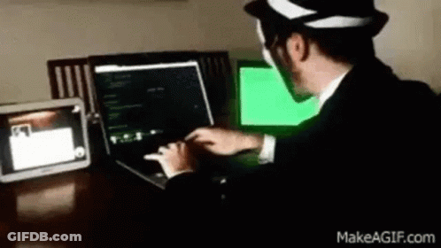 A Man In A Suit And Hat Is Typing On A Laptop Computer . GIF