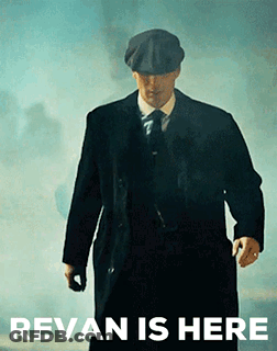 A Man In A Suit And Hat Is Walking In Front Of A Sign That Says ' Revan Is Here ' . GIF