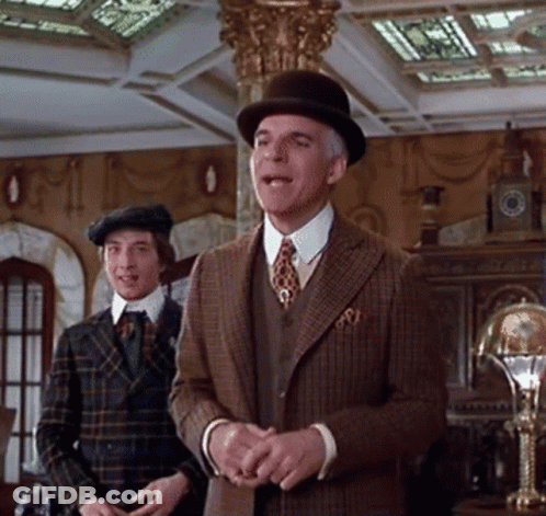 A Man In A Suit And Hat Stands Next To Another Man In A Plaid Suit GIF