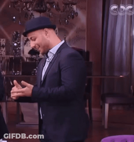 A Man In A Suit And Hat Talks To A Woman In Front Of A Cdg Sign GIF