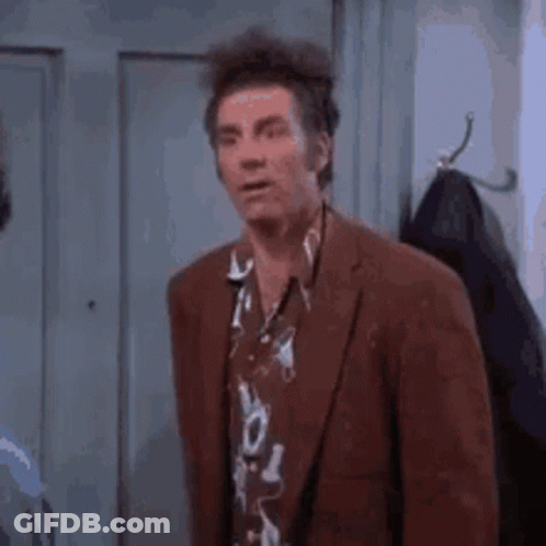 A Man In A Suit And Hawaiian Shirt Is Standing In Front Of A Locker . GIF