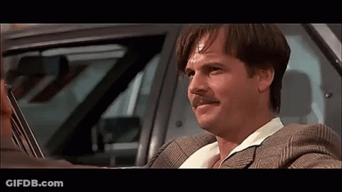 A Man In A Suit And Mustache Is Driving A Car . GIF