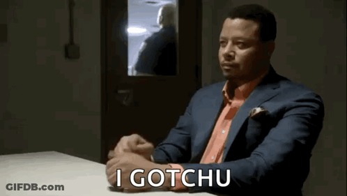 A Man In A Suit And Orange Shirt Is Sitting At A Table With The Words `` I Gotchu '' Written On It . GIF