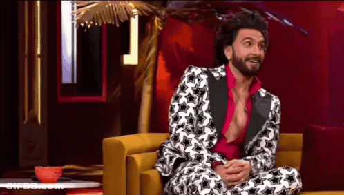 A Man In A Suit And Pink Shirt Is Sitting On A Couch . GIF