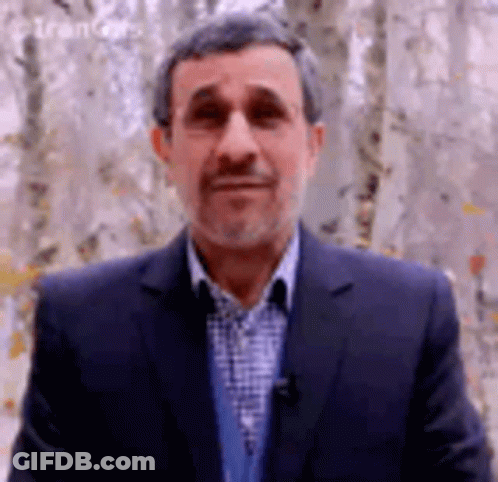A Man In A Suit And Plaid Shirt Is Standing In Front Of A Forest . GIF