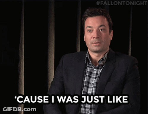 A Man In A Suit And Plaid Shirt Is Waving His Hand In Front Of A Black Curtain With #Fallontonight Written On It GIF
