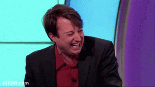 A Man In A Suit And Red Shirt Is Laughing On A Stage GIF