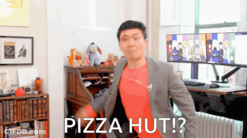A Man In A Suit And Red Shirt Is Standing In Front Of A Desk With The Words Pizza Hut On It GIF
