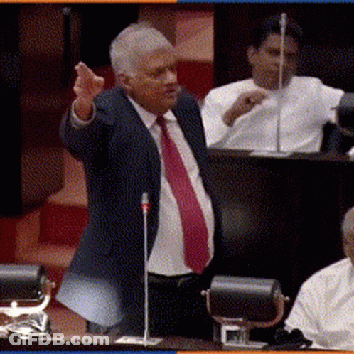 A Man In A Suit And Red Tie Is Speaking Into A Microphone GIF