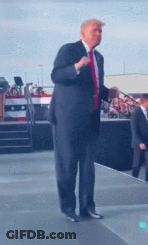 A Man In A Suit And Red Tie Is Standing On A Stage GIF