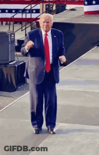 A Man In A Suit And Red Tie Is Standing On A Stage GIF