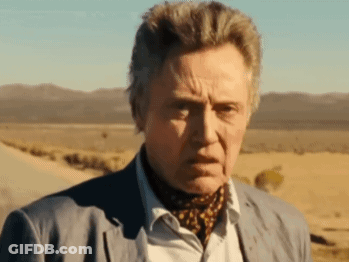 A Man In A Suit And Scarf Is Standing In A Desert GIF