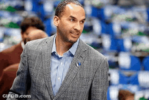 A Man In A Suit And Striped Shirt Is Standing In Front Of A Crowd . GIF