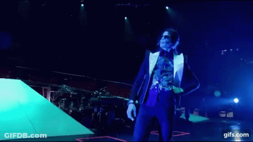 A Man In A Suit And Sunglasses Is Dancing On A Stage In Front Of A Microphone . GIF
