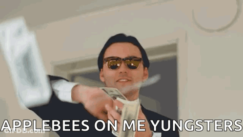 A Man In A Suit And Sunglasses Is Holding A Bunch Of Money And Says Applebees On Me Yungsters GIF