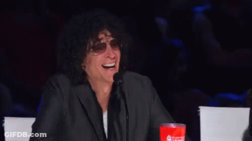 A Man In A Suit And Sunglasses Is Laughing While Sitting At A Table . GIF