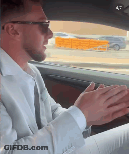 A Man In A Suit And Sunglasses Is Sitting In A Car With His Hands Folded In Front Of Him GIF