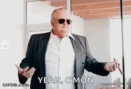 A Man In A Suit And Sunglasses Is Smoking A Cigar And Saying `` Yeah , C 'Mon '' . GIF