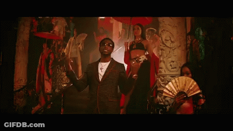 A Man In A Suit And Sunglasses Is Standing Next To A Woman In A Bikini And Holding A Fan . GIF