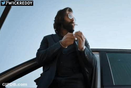 A Man In A Suit And Sunglasses Smoking A Cigarette In A Car With The Twitter Username 7Wickreddy Below Him GIF