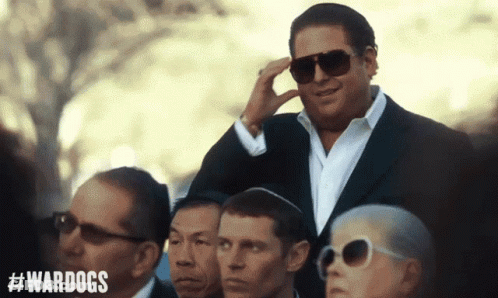 A Man In A Suit And Sunglasses Stands In A Crowd With #Wardogs On The Bottom GIF
