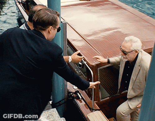 A Man In A Suit And Sunglasses Talks To Another Man In A Boat GIF