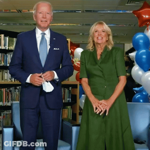 A Man In A Suit And Tie And A Woman In A Green Dress Stand Next To Each Other GIF