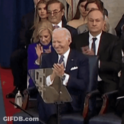 A Man In A Suit And Tie Applauds While Sitting In A Crowd GIF