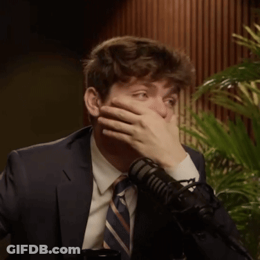 A Man In A Suit And Tie Covers His Mouth With His Hand GIF