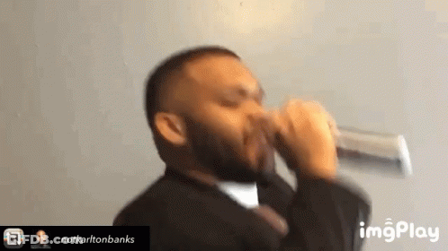 A Man In A Suit And Tie Drinking From A Glass . GIF