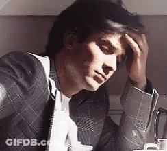 A Man In A Suit And Tie Has His Hand On His Forehead GIF