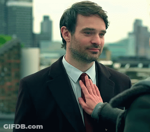 A Man In A Suit And Tie Has His Hand On His Tie GIF