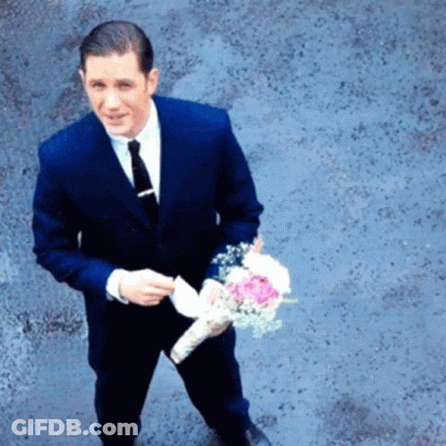 A Man In A Suit And Tie Holding A Bouquet Of Flowers GIF