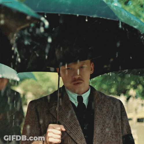 A Man In A Suit And Tie Holding An Umbrella GIF
