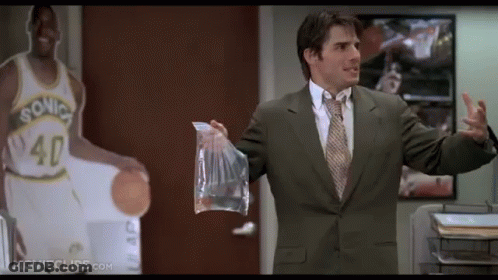 A Man In A Suit And Tie Holds A Bag In Front Of A Sonics Basketball Player GIF