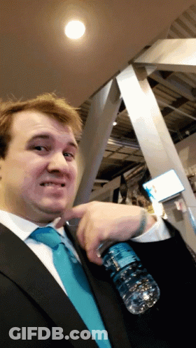 A Man In A Suit And Tie Holds A Bottle Of Water In His Pocket GIF