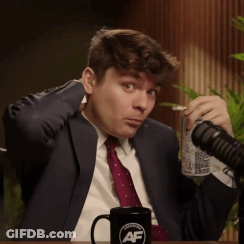 A Man In A Suit And Tie Holds A Can Of Soda In Front Of A Microphone And A Mug That Says American Af GIF