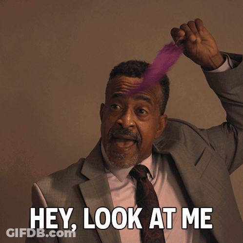 A Man In A Suit And Tie Holds A Feather In His Hair And Says " Hey Look At Me " GIF