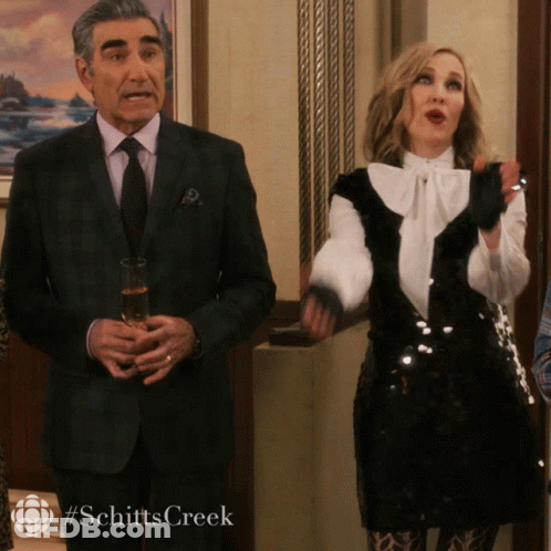 A Man In A Suit And Tie Holds A Glass Of Champagne Next To A Woman In A Black And White Sequined Dress GIF