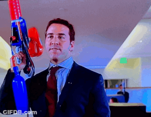 A Man In A Suit And Tie Holds A Large Toy Gun GIF