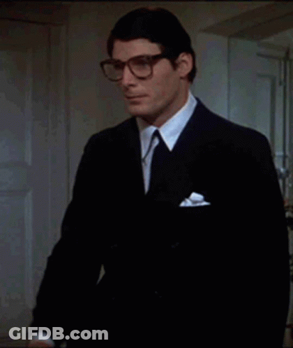 A Man In A Suit And Tie Holds A Pair Of Glasses In His Hand GIF