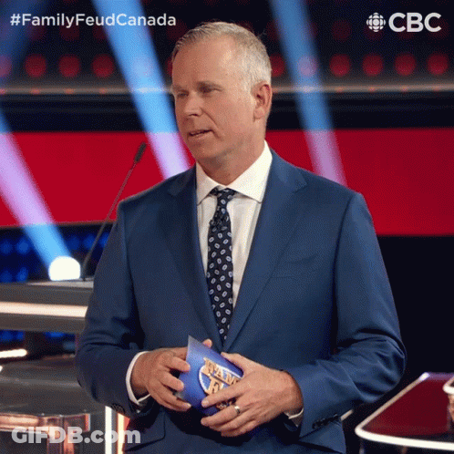 A Man In A Suit And Tie Holds A Piece Of Paper That Says Family Feud Canada On It GIF