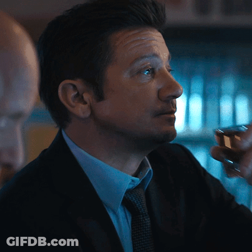 A Man In A Suit And Tie Holds A Small Glass GIF