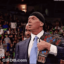 A Man In A Suit And Tie Holds A Wrestling Belt Over His Shoulder GIF