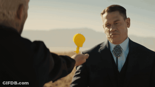 A Man In A Suit And Tie Holds A Yellow Object In His Hand GIF